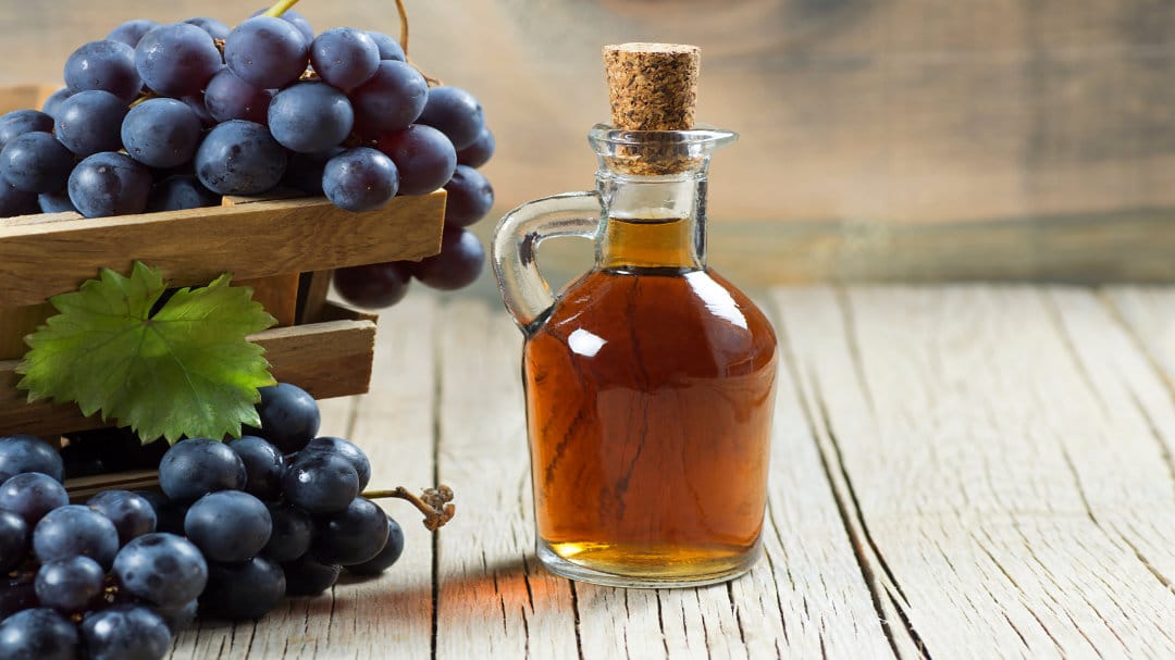 Eine Flasche Traubenessig steht auf einem Holztisch umgeben von Weintrauben