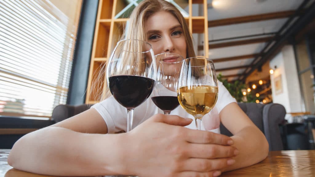 Eine Frau sitzt an einem Tisch vor drei Gläsern Wein